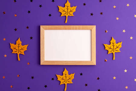 Yellow felt autumn leaves star shapes and wooden picture frame on purple background with copy space. Halloween scary holiday and autumn conceptの写真素材