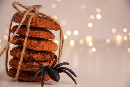 Close up of oatmeal cookies in a stack tied with brown thread and halloween black spider on bright background with bokeh. Sweet food concept with copy spaceの写真素材