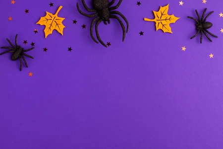 One big and two tiny black artificial spiders stars and yellow felt leaves on purple background with copy space. Halloween scary holiday and autumn conceptの写真素材