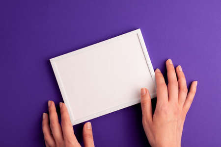 Mockup white frame with white paper inside and human hands on it on vibrant purple background....