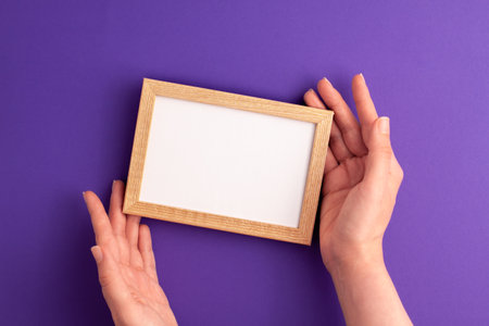 Mockup wooden frame with white paper inside and human hands on it on vibrant purple background. Halloween holiday presents happy birthday concept with space for your text template flat lay.の写真素材