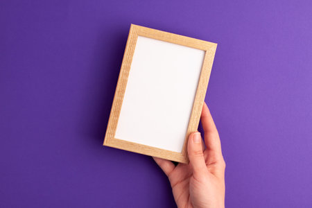 Mockup wooden frame with white paper vertical inside and human hands on it on vibrant purple...