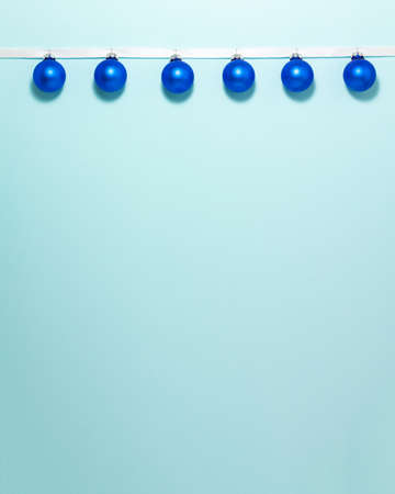 Dark blue christmas balls on white ribbon at the top side on blue background. Christmas winter...