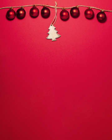 Red christmas balls on thread and in the middle is a wooden Christmas tree with glitters on the tips on the top side on red background. Flat lay top view with copy space. Holiday conceptの写真素材