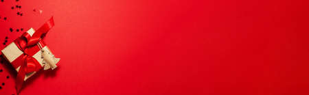 Banner of brown paper gift box with a red satin ribbon bow with wooden tree and stars on top on red Christmas holiday mother and father Valentines days birthday present flat lay concept copy spaceの写真素材