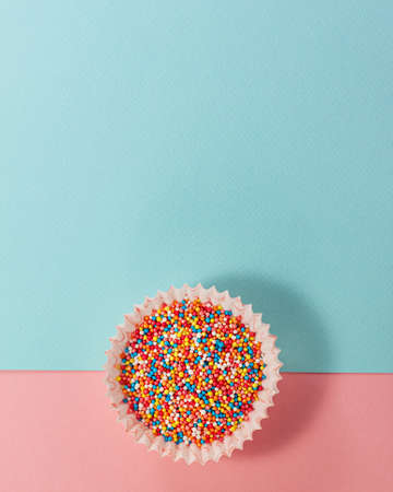 Cupcake liner with colored sugar inside at the bottom from above. Flat lay top view. Confectionery cooking concept on bright pink and blue paper background. National cooking dayの写真素材