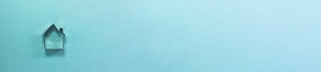 Banner of steel house shaped cutter for cookies from above. Flat lay top view. Confectionery cooking concept with copy space on bright blue paper backgroundの写真素材