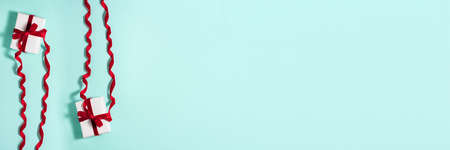 Banner of two white paper gift boxes with a red satin ribbon bow on top on blue background. Christmas holiday mother and father Valentines days and birthday present flat lay concept with copy spaceの写真素材