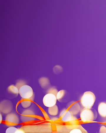 Close up of an orange satin ribbon bow at the bottom with golden bokeh on vibrant purple blurred background with copy space. Holiday presents and Halloween conceptの写真素材