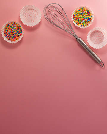 Cupcake liners with colored sugar inside whisk from above flat lay top view. Confectionery cooking concept with copy space on bright pink paper background National cooking dayの写真素材