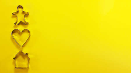 Banner of steel house heart and men shaped cutter for cookies on the left from above. Flat lay top view. Confectionery cooking concept with copy space on bright yellow paper backgroundの写真素材