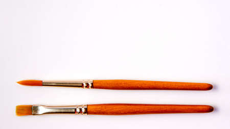Flat lay of artistic orange metal wooden paint brushes close up on white background with copy space from above. Drawing and design concept work tools on the bottomの写真素材