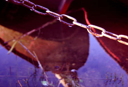 Locked boat in a dock. Close-up of the chain, reflection of the boats in the waterの写真素材