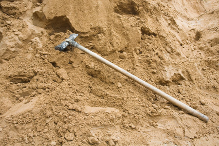 Construction sand pile with iron shovel, beside paved road. High quality photoの写真素材