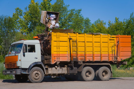 A large recycling truck is seen here, likely on a collection route. The truck's arm is lifting a trash can, and the can's contents are spilling into the truck's open hopper.の写真素材