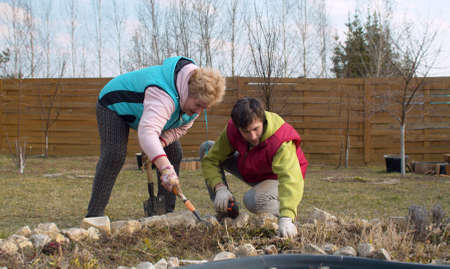 Senior mom and young adult son working together in the spring garden. They are smiling. Family relations conceptの写真素材
