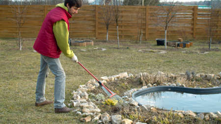 Spring work in the garden. Young man raking last years dry grass on a flower bed. Eco friendly. Earth day.の写真素材