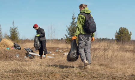 Two young eco volunteers picking plastic. Early spring, the garbage that was covered with snow is...