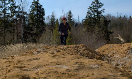 Young man running on a sand hill near the forest. Early spring, sunny weather. Bright blue sky, no leaves on the trees, green young fir-trees. Healthy lifestyle conceptの写真素材
