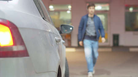 Close up car and young handsome man against the building of the gas station. Daily city life
