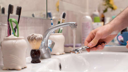 Close-up male hands washing shaving machine in a sink with water. Bright bathroom closeup. Daily face careの写真素材