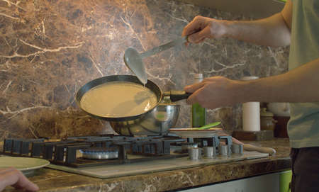 Close up young man frying pancakes. He pouring dough into a pan. Domestic daily life, togetherness, family.の写真素材
