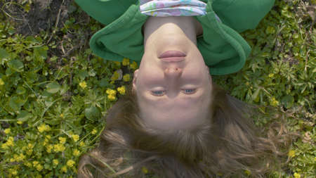 Top view close up portrait of cheerful woman laying on the grass in the forest. Camera rotating, she smiling and squinting. Early spring, sunny weather. Healthy lifestyle conceptの写真素材