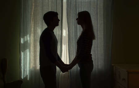 Silhouette of couple near the window. Family holding hands. The curtains are closed in the roomの写真素材