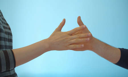 Close up hands of young couple playing rock paper scissors on blue background indoors.