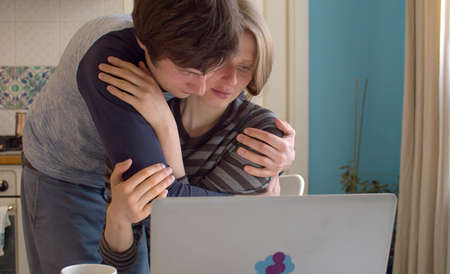 Young couple hugging. Portrait of a young woman working from home at the kitchen. Couple in love at home, remote job.の写真素材