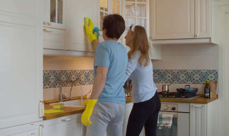 Funny happy family cleaning kitchen. They soaping the kitchen cabinets in synchronized movements. Togetherness, domestic daily life, housekeepingの写真素材