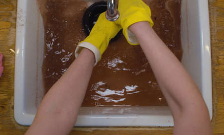 Close up female hands in protective gloves cleaning a blockage in a kitchen sink with a plunger....