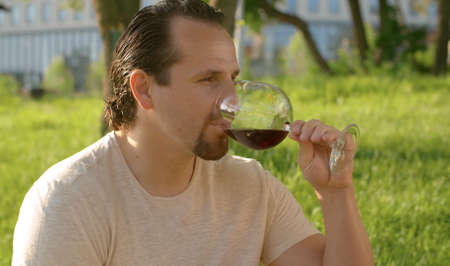 Close up portrait of a handsome smiling man with a glass of wine in his hands. He is tasting and...