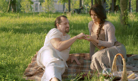 Happy couple sitting on blanket in the park. Man gently caresses a womans hand. Picnic on the grass. Love, pleasure, relaxation and togetherness conceptの写真素材