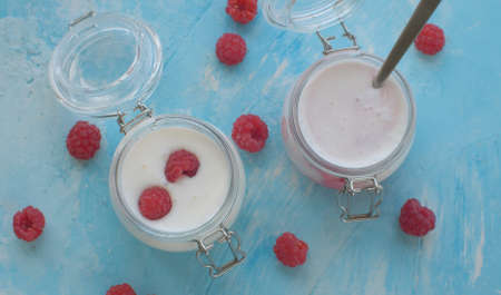 Close up two jars of yogurt with fresh raspberries. Top view, blue backgroundの写真素材