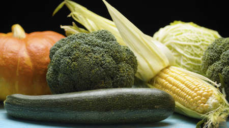 Close up fresh raw vegetables - cabbage, broccoli, pumpkin, zucchini and an ear of corn on the table on black backgroundの写真素材