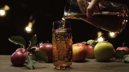 Close up hand pouring fresh apple juice into glass and delicious red apples against black background. Healthy food, vitamins, fruitsの写真素材
