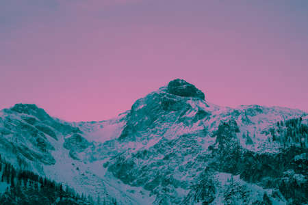 Photo depicting a beautiful colorful moody frosty landscape European alpine mountains with snow peaks on a cloudy sky background. Vintage hipster pink and blue duo tone filter.の写真素材