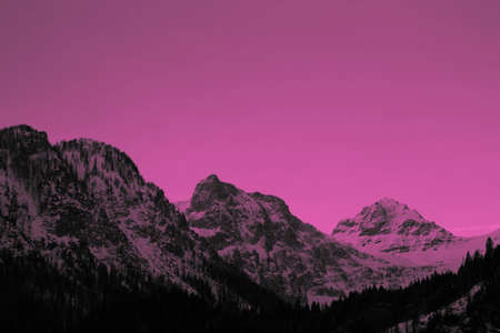 Photo depicting a beautiful colorful moody frosty landscape European alpine mountains with snow peaks on a cloudy sky background. Vintage hipster pink tone filter.の写真素材