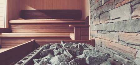 Wooden Bathhouse with a heating pot filled with stones, close up. Wooden sauna interior with equipment.の写真素材