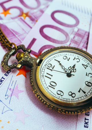 Old pocket watch with euro banknotes money, macro view. Time and business concept.の写真素材