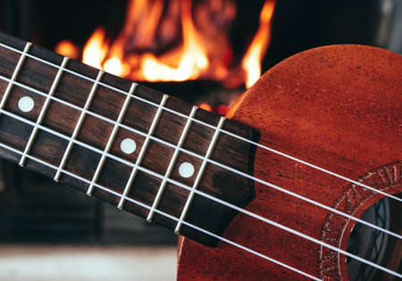 Ukulele small guitar close up stings, fireplace on the background. Musical concept, guitar fret...