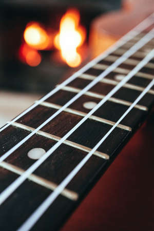 Ukulele small guitar close up stings, fireplace on the background. Musical concept, guitar fret...