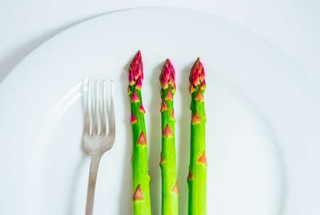 Fresh green asparagus sprouts, on a plate with a fork. Two asparagus stems, isolated on white background, macro.の写真素材