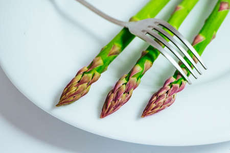 Fresh green asparagus sprouts, on a plate with a fork. Two asparagus stems, isolated on white background, macro.の写真素材
