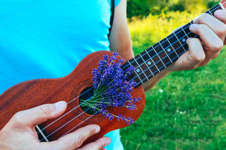 A musical instrument guitar, decorated with lavender flowers, in the hands of a player. Musician fingers are playing on the guitar, outdoor natural background.の写真素材
