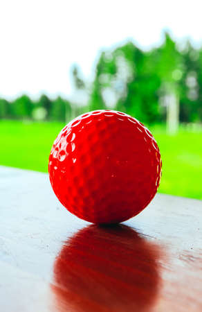 Golf red ball on a wooden surface, green field and blue sky. Macro view, luxury sport concept.の写真素材