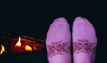 Burning wood at the fireplace, female legs in socks warming up. Firewood bricks at the fire, woman foot heating.の写真素材