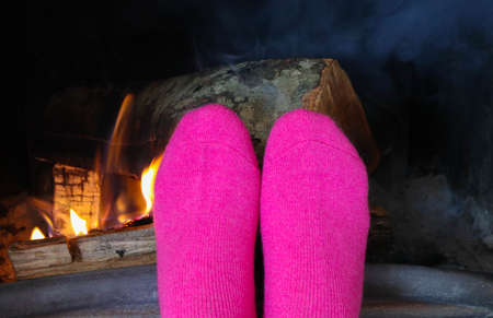 Burning wood at the fireplace, female feet in pink socks warming up. Firewood bricks at the fire, woman foot heating.の写真素材