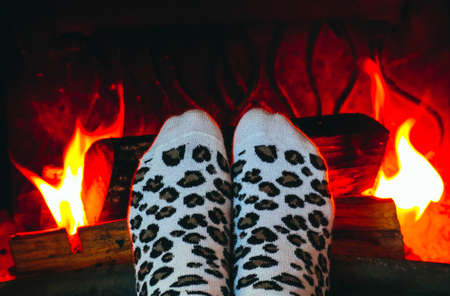 Burning wood at the fireplace, female legs in socks warming up. Firewood bricks at the fire, woman foot heating.の写真素材